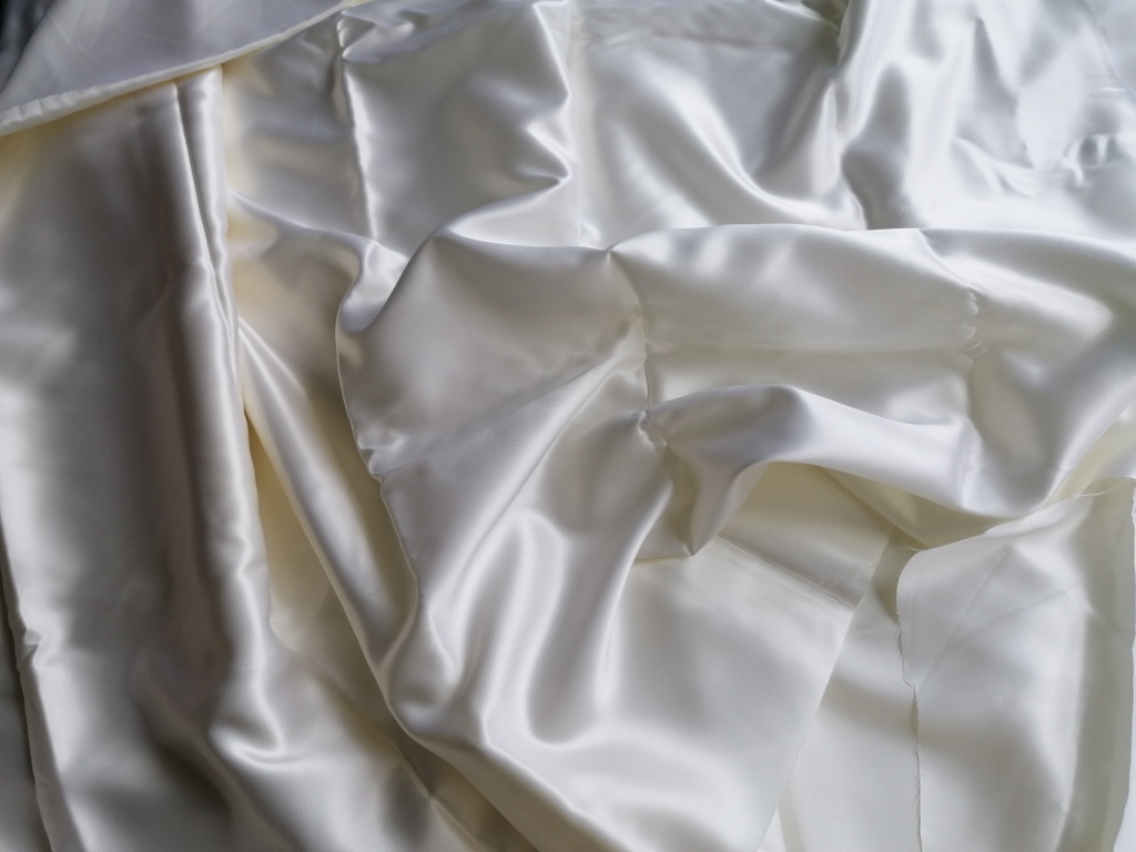 Dikke satijn gebroken wit met mooie glans, gedrapeerd in plooien