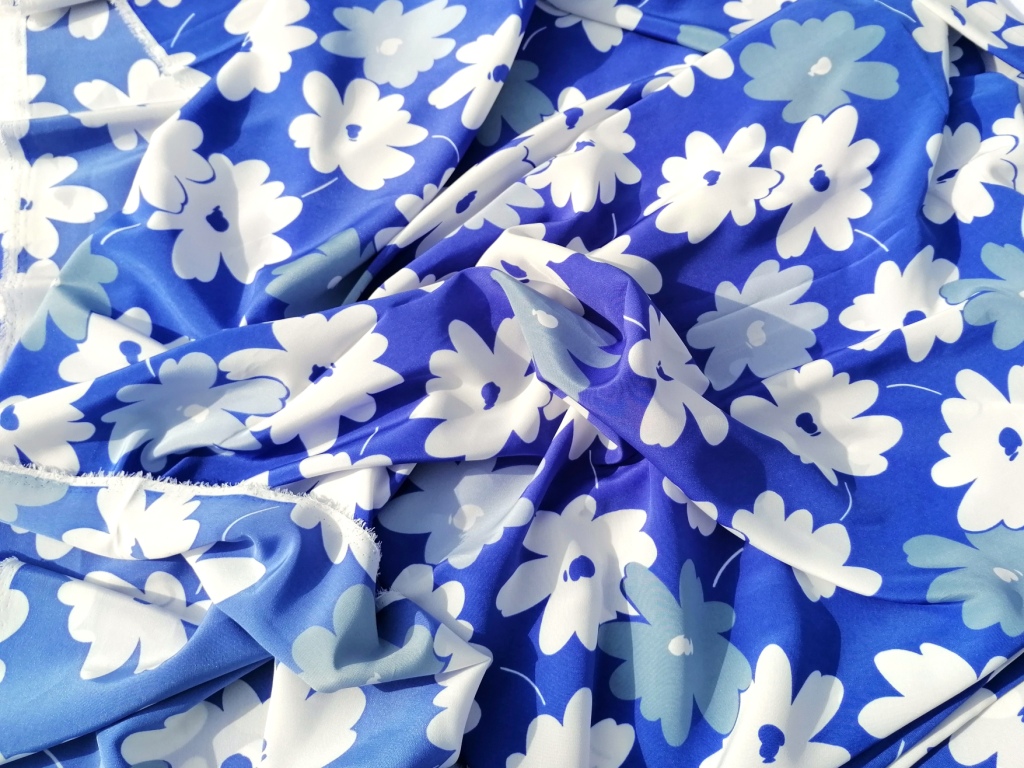Soepele stof blauw wit gebloemd gedrapeerd, vloeiende val en blauwe ondergrond met witte bloemen zichtbaar