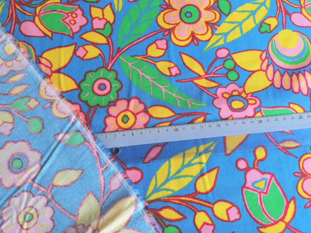 Detailopname van de bloemprint: gele, roze en groene bloemen op lichtblauwe ondergrond.